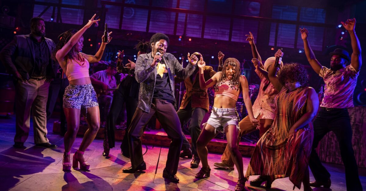 The company mid-number under stage light, the whole ensemble dancing together